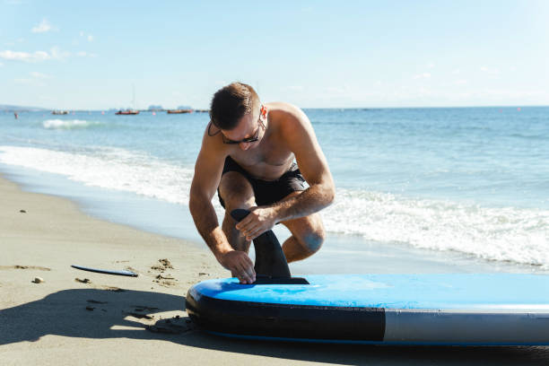 istock Young male surfer setting up standup paddleboard on a beach. 1389293135