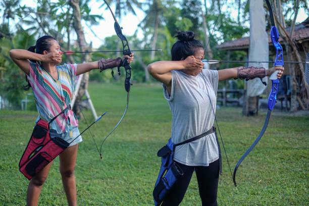 Close-up shot of two female friends practicing archery in the outdoor shooting range.