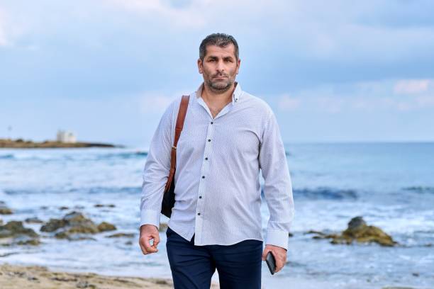 istock Serious confident successful mature man walking along the beach. 1389296867