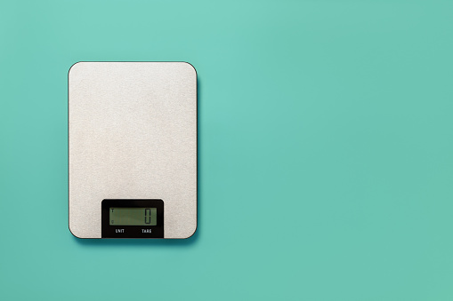 Digital kitchen scales against turquoise background. Electronic scales for food weight measurement. Design element for dieting and cooking concepts. Household measuring device. Copy space.