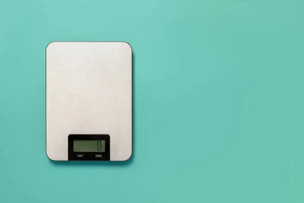 Digital kitchen scales against turquoise background. Electronic scales for food weight measurement. Design element for dieting and cooking concepts. Household measuring device. Copy space. Top view.