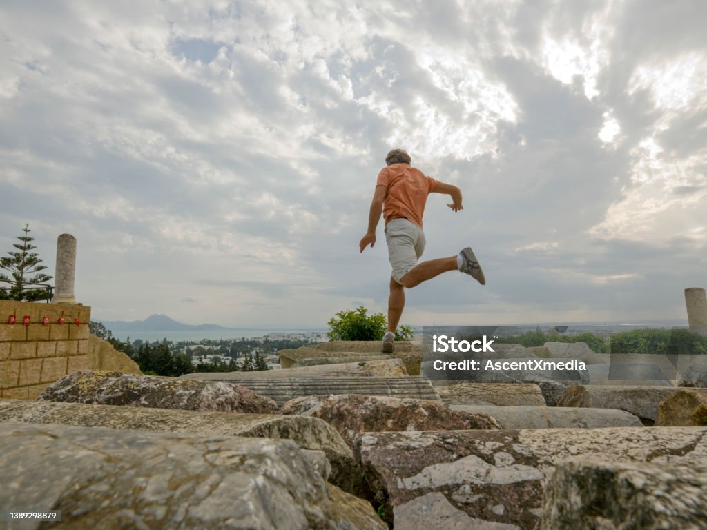 Man jumps between rocks below moody sky Carthage ruins Carthage - Tunisia Stock Photo