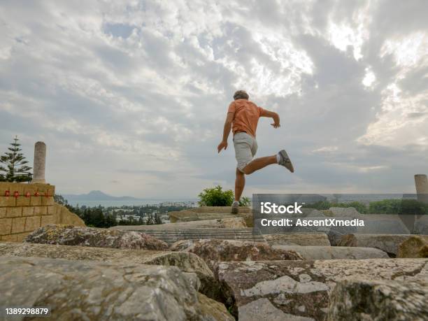 Man Jumps Between Rocks Below Moody Sky Stock Photo - Download Image Now - Carthage - Tunisia, Jumping, The Way Forward
