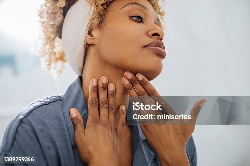istock Pretty Woman Applying Face Cream on her Neck 1389299366