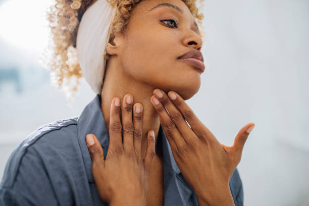 Pretty Woman Applying Face Cream on her Neck Beautiful woman looking away and touching her neck with her hands. She is standing in her bathroom. She is probably putting face cream on her neck. hair care women mature adult human skin stock pictures, royalty-free photos & images