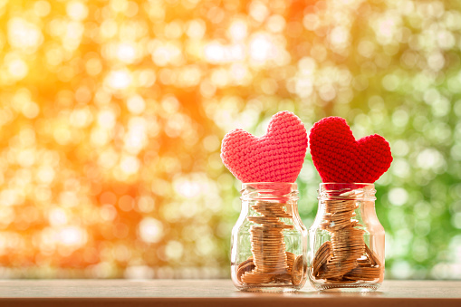 Keep a gold coin in the two clear bottle with growing value as a red and pink hearts on the top on bokeh background in the public park, Saving money for buy health insurance to the loved ones concept.
