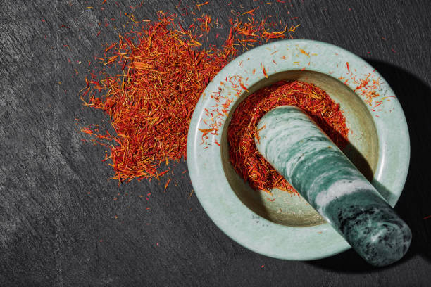 Saffron in a marble mortar on a dark stone background, top view, seasoning preparation. Aromatic spices and seasonings