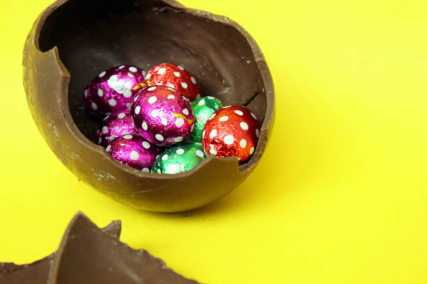 A cracked chocolate Easter egg with colorful little round candies inside. Happy Easter. Chocolate. Sweets for children and adults. Candy. Dessert. Copy space. Top view. Flat lay.