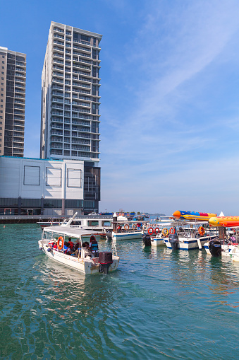 Kota Kinabalu, Malaysia - March 17, 2019: White motorboats with passengers are near the Jesselton Point ferry terminal on a sunny day, vertical photo