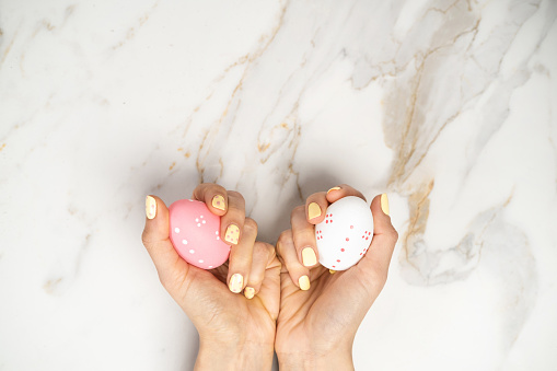 Close up on spring manicure, yellow with pink dots, hand holding pastel pink Easter egg decoration.