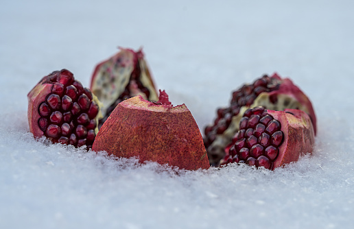 Slices of ripe pomegranate in the snow. close-up. white fluffy snow around a red pomegranate. Useful fruits for maintaining health. Ripe ruby beans