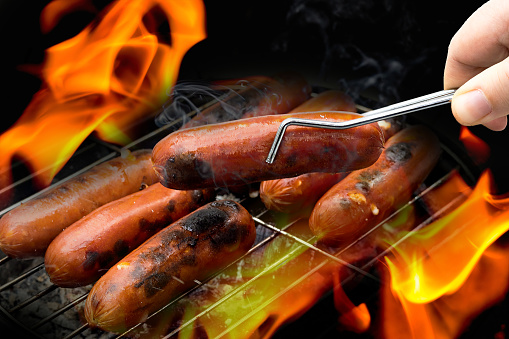 Fried sausages on barbecue charcoal grill in fire.