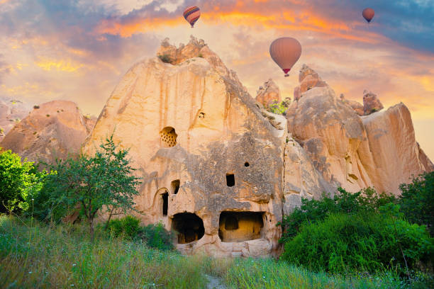 Rock monastery in Zelve valley under dramatic sky with hot air balloons stock photo