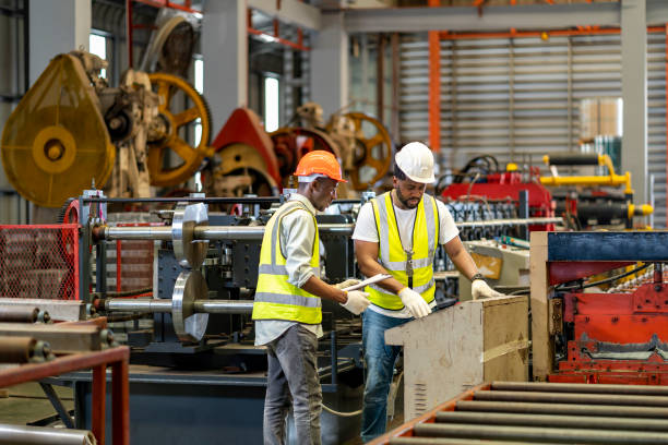 un team di operai industriali afroamericani sta controllando il valore di installazione della macchina per la formatura del rotolo di lamiera metallica tramite monitor automatizzato mentre lavora all'interno della fabbrica del tetto per il concetto di indu - operaio di produzione foto e immagini stock