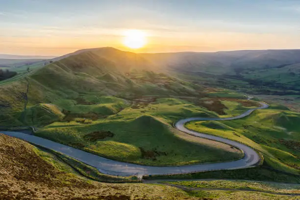 A long and winding rural road leading through lush green British countryside on a beautiful Summer evening. Taken from Mam Tor in the Peak District, UK.