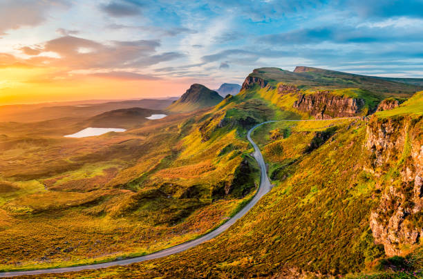 Long winding road at Quiraing on the Isle of Skye with a beautiful vibrant sunrise sky. A beautiful vibrant sunrise looking towards The Trotternish Ridge, seen from the iconic Quiraing on The Isle of Skye! A single lane rural road can be seen winding up the mountain side. winding road mountain stock pictures, royalty-free photos & images
