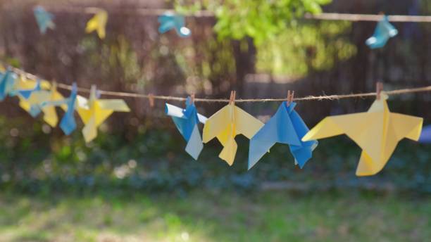 carta origami blu e gialla decorazione delle colombe della pace appesa nel parco come segno di sostegno all'ucraina durante la guerra con la russia dopo l'invasione - pacifism foto e immagini stock