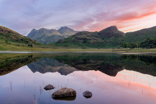 Beautiful reflections of sunrise sky in water with a stunning view of The Langdale Pikes mountain range. Blea Tarn, Lake District, UK.