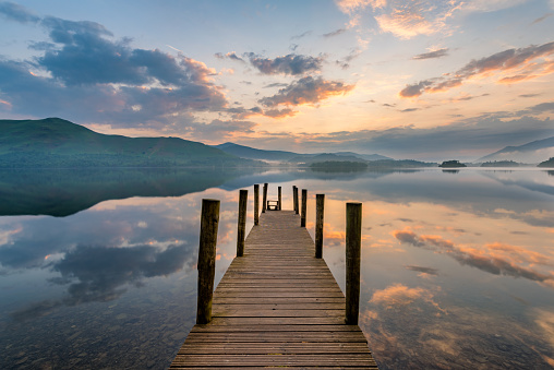 Long wooden jetty with poles leading out to lake at sunset in the Lake District, UK.