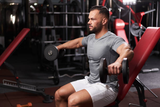 Bodybuilder doing shoulder workout Young man in the gym doing shoulder workout with dumbbells deltoid stock pictures, royalty-free photos & images