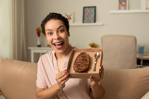Happy woman showing stuffed chocolate easter egg at home.