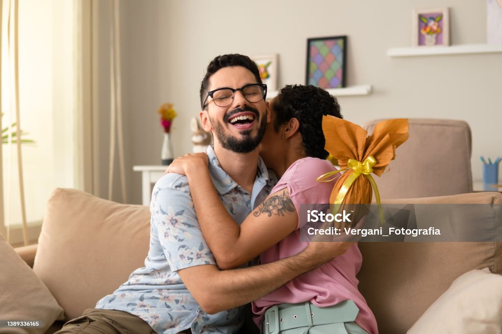 man hugging woman with golden easter egg Happy man hugging woman with golden easter egg in hand at home Easter Stock Photo