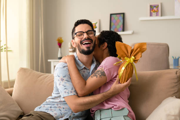 man hugging woman with golden easter egg Happy man hugging woman with golden easter egg in hand at home easter sunday photos stock pictures, royalty-free photos & images