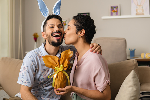 Man with bunny ear giving easter egg. Woman kissing boyfriend in the cheek