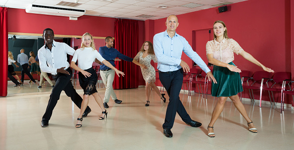 Smiling people learning tap dance movements in dancing class