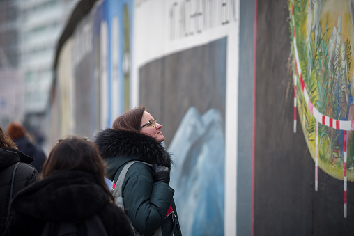 February 27, 2022 - Berlin, Germany:  Tourists watching a Fragment of East Side Gallery in Berlin, Germany. It's a 1.3 km long part of original Berlin Wall which collapsed in 1989, and now is the largest world amateur art gallery of graffiti