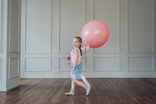 A girl with a big pink balloon playing indoors. Cheerful kid holding a balloon
