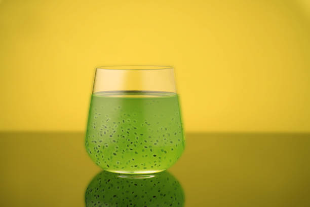 Green drink with black seeds in a pyramidal glass on a yellow background.