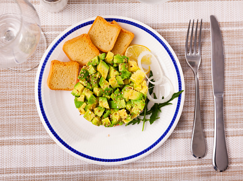 Popular dish of French cuisine is salmon tartar with avocado, served with a slice of lemon and croutons