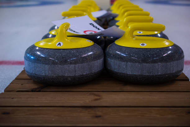istock Curling stones with a yellow handle sit on a wooden base. 1389346039