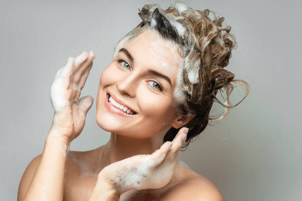 young cheerful woman is washing her hair with a shampoo - shampoo imagens e fotografias de stock