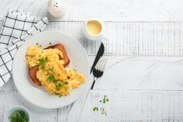 istock Scrambled Eggs. Fluffy and Buttery scrambled eggs on bread with microgreen radish and hollandaise sauce on white plate over white wooden background. Homemade breakfast or brunch meal. Top view. 1389348796