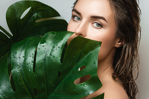 Portrait of beautiful young woman with a smooth skin holding Monstera deliciosa plant leaf