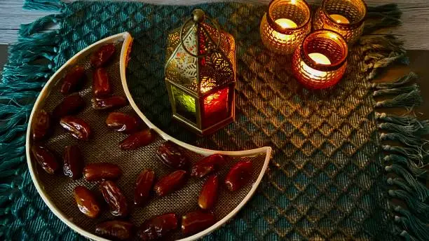 A half moon shaped tray with dates and an oriental lamp with three little tea light holder on a green mat for Ramadan decoration