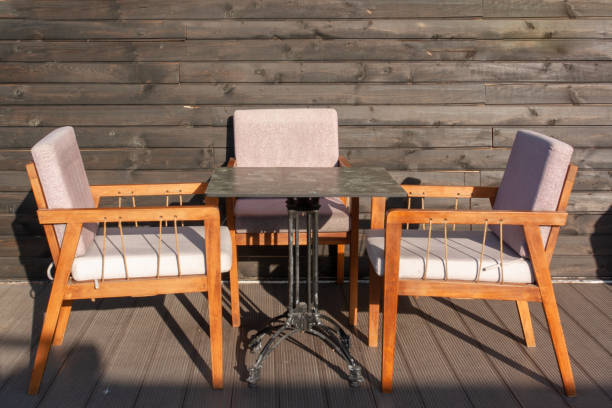 Table and three soft chairs in cafe against wooden black wall.
