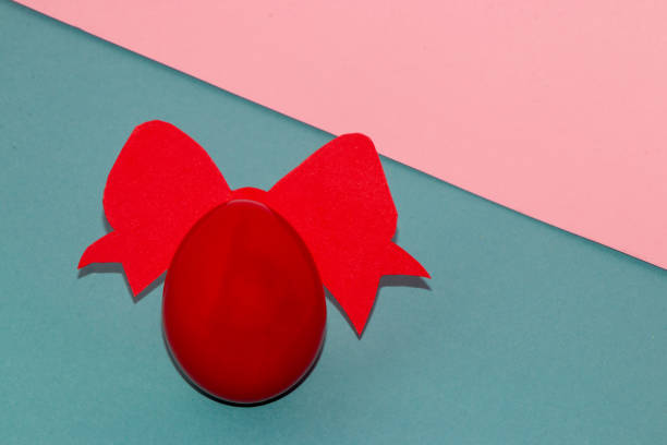red egg with red bow on pastel blue pink background, copy space, creative art easter composition, beautiful design
