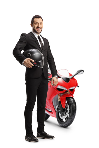 Full length portrait of a businessman holding a helmet and posing with a red motorbike isolated on white background