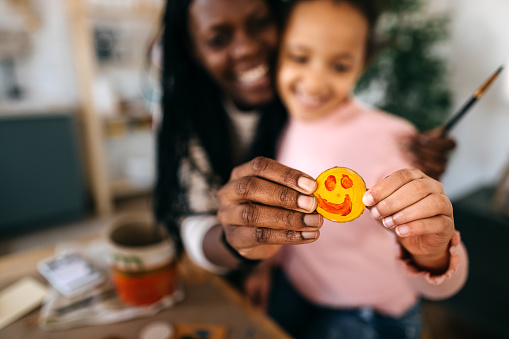 Close-up of mother and daughter hands holding small wood with anthropomorphic smiley face at home