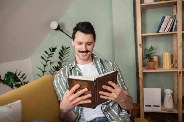 istock Young man sitting on the sofa, engrossed in reading a book 1389364926