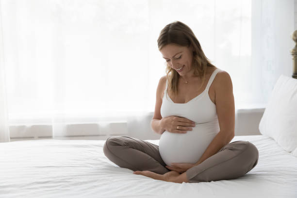 istock Happy expectant mother sitting on bed, feeling kicks 1389365385