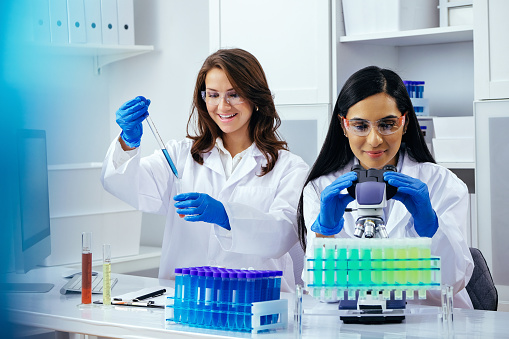 Two beautiful young female scientists working in laboratory with test tubes and microscope doing some research pharmaceutical