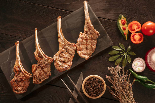 Cooked Lamb Chops Prepared on a Dark Slate Cutting Board with a Ramekin or Pesto on the side with Rosemary and other herbs stock photo