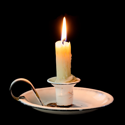 Burning candle in old vintage enamel candle holder with handle, isolated on black background.