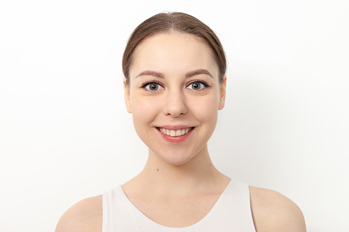 Close-up studio portrait of an attractive 20 year old woman with brown hair in a white tank top on a white background
