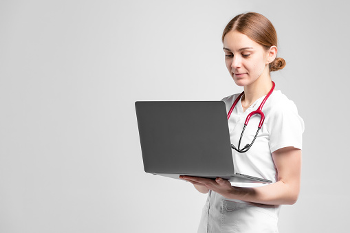 Female portrait of professional doctor at the studio. Woman working on laptop computer for telemedicine. Concept on isolated background.