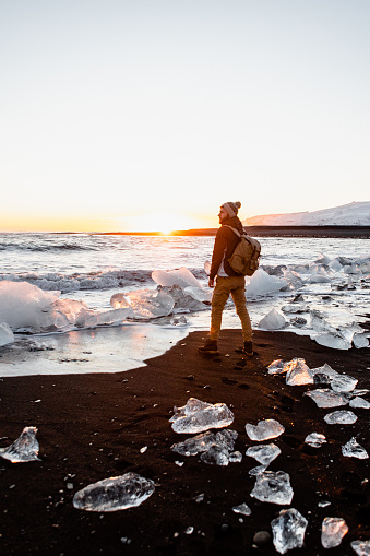 The male traveler standing and looking towards the sunset at the Diamond beach in Iceland